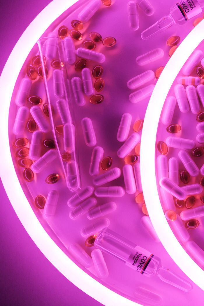 Top view of different pills and capsules near vaccine for coronavirus in bright pink neon light